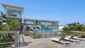 A Fire Island glass house drew 350+ viewers at $5.25 million but no buyer; after $1.255 million in cuts, its $3.995 million ask is still nearly $1.3 million above Cherry Grove’s record sale